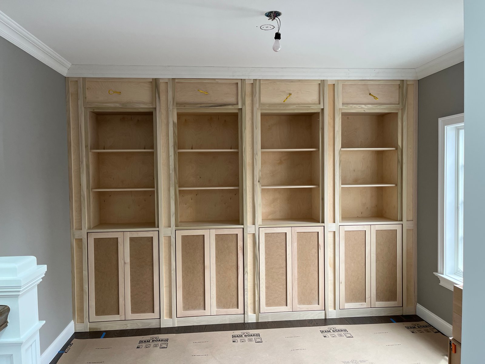 Before painting: four bays of bare wood shelving and lower cabinet doors