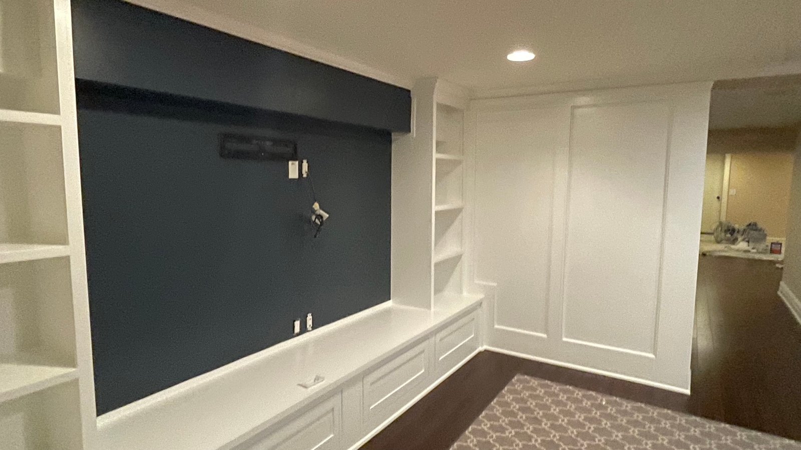 After painting: the same shelves and paneling in white, with a navy TV wall and exposed TV wiring