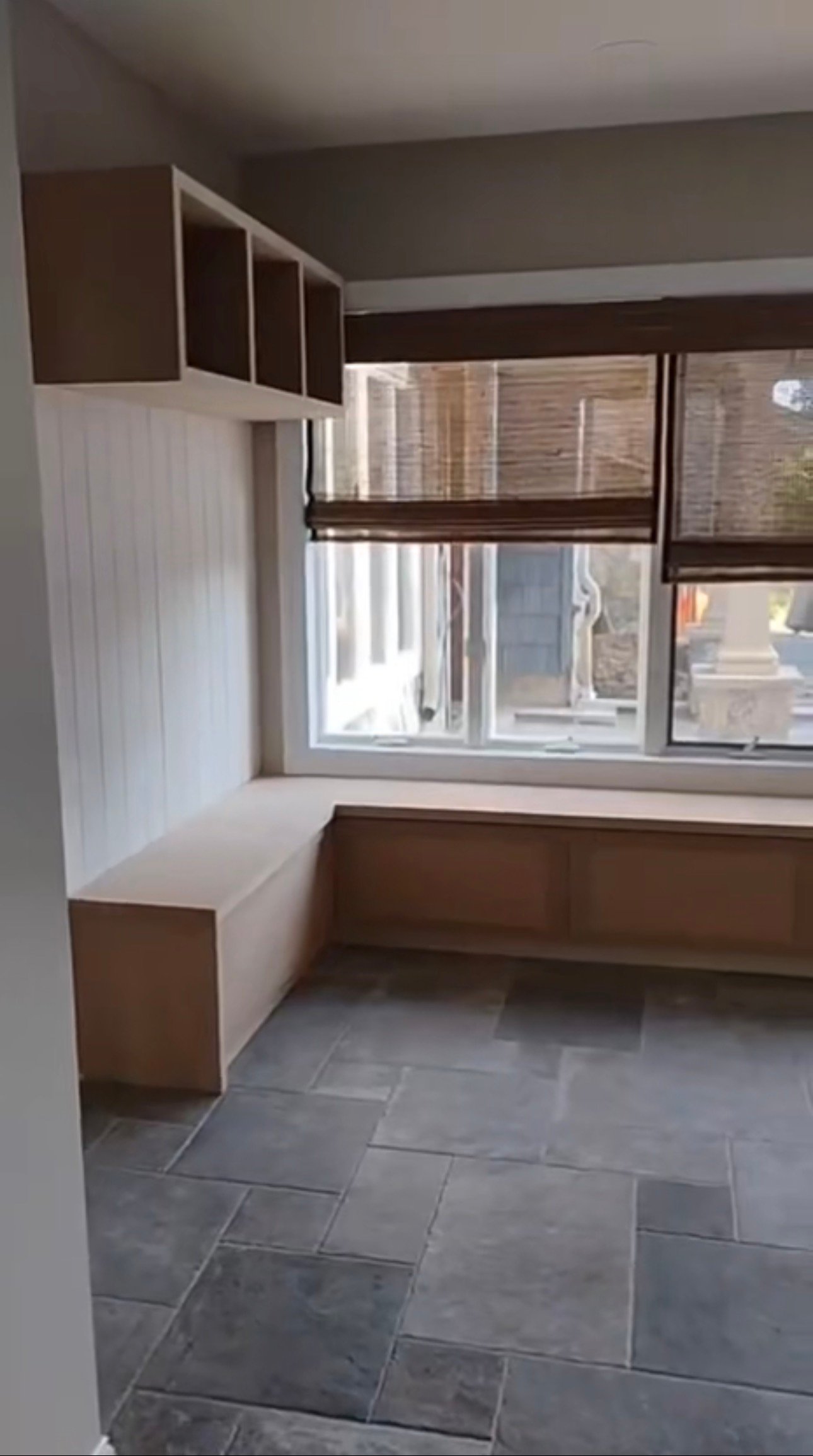 Before painting: unfinished mudroom bench, cubbies and wall paneling beside the window