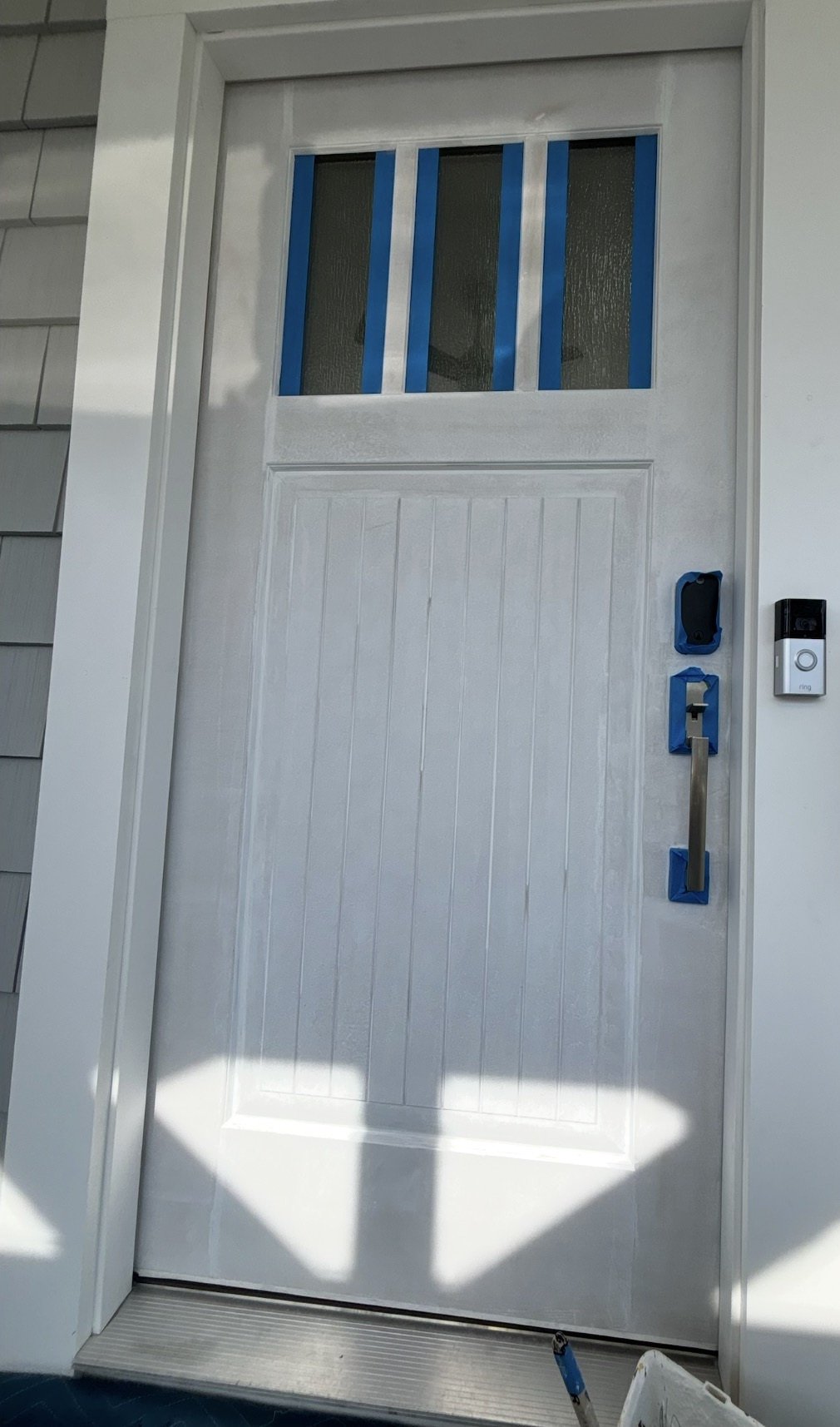Before painting: primed white front door with glass and hardware taped